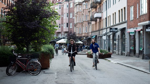 Två personer cycklar fram i Malmömiljö mot kameran.