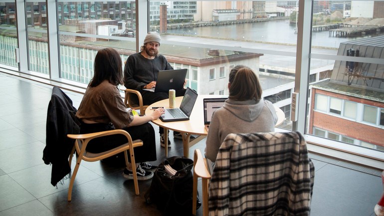 Studenter pluggar tillsammans framför stort fönster.