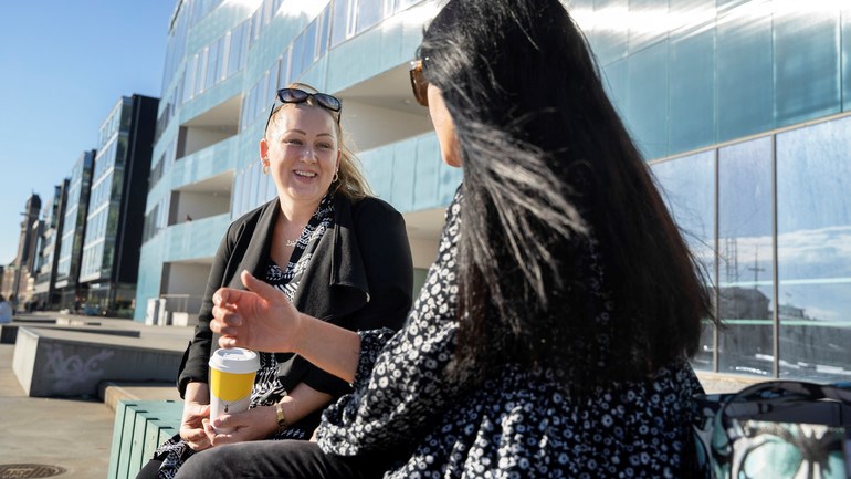 Studenter fikar i solen utanför universitetet.