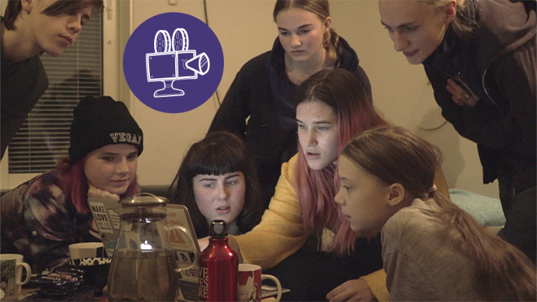 The actors in the film are sitting around a table, looking at a computer screen.