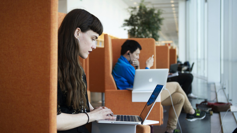 Studenter i orangea fåtöljer med laptops i knäet