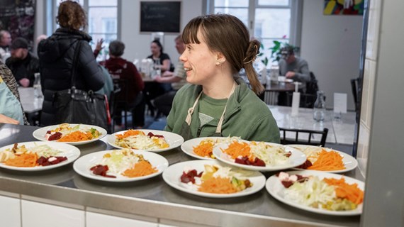 Två personer med förkläde gör sig redo att servera mat i föreningslokal.