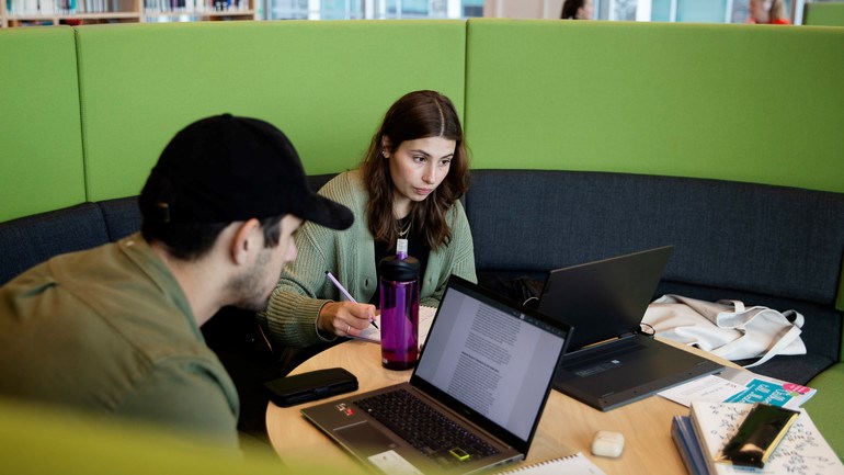 Två studenter med gröna tröjor sitter i grön soffa i Orkanenbiblioteket.