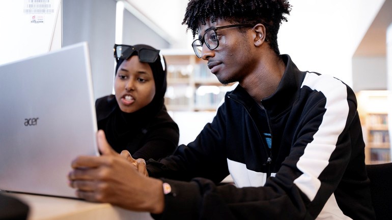 Studenter arbetar framför datorer i biblioteket.