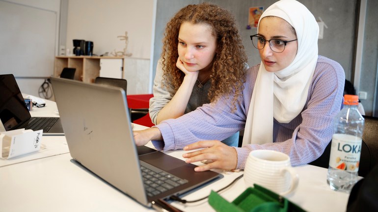 Två personer sitter vid ett bord med en bärbar dator.