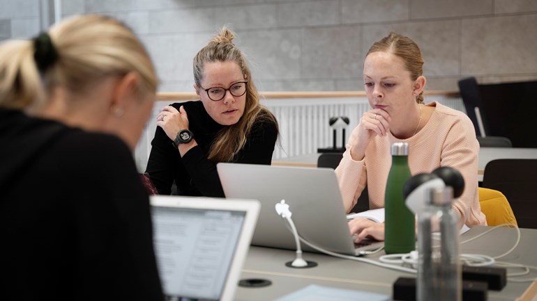 Tre studenter sitter runt ett bord och tittar på datorer.