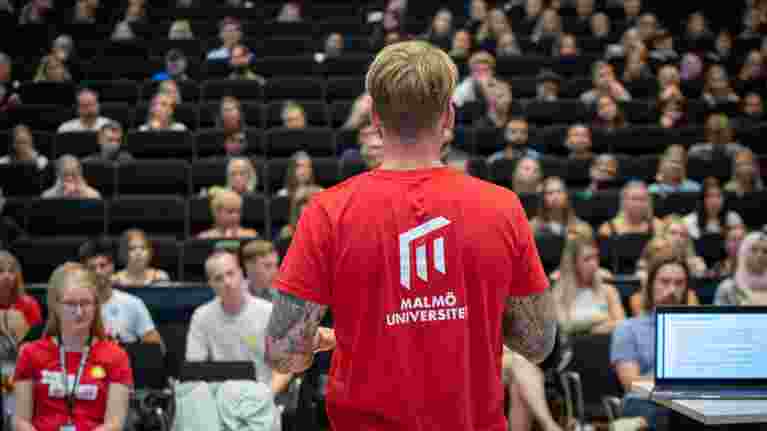 Person in Malmö University T-shirt presenting in auditorium.