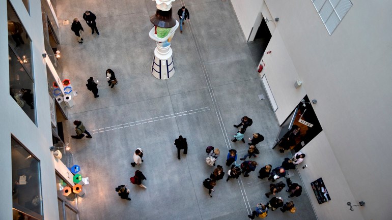 Människor rör sig i Orkanens atrium. I mitten av atriumet reser sig en entrépelare.
