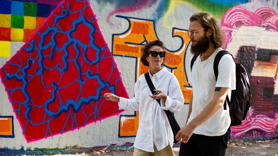 Två personer med vita kläder promenerar framför grafittivägg.