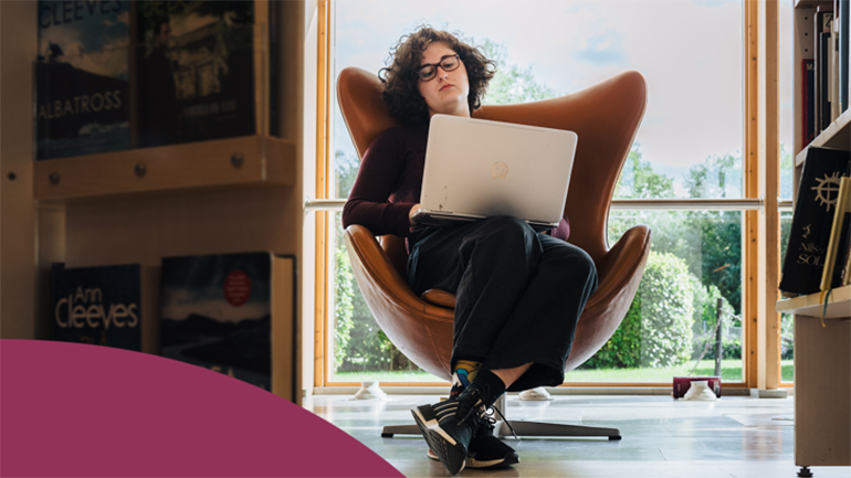 Student sitter i fåtölj med laptop.